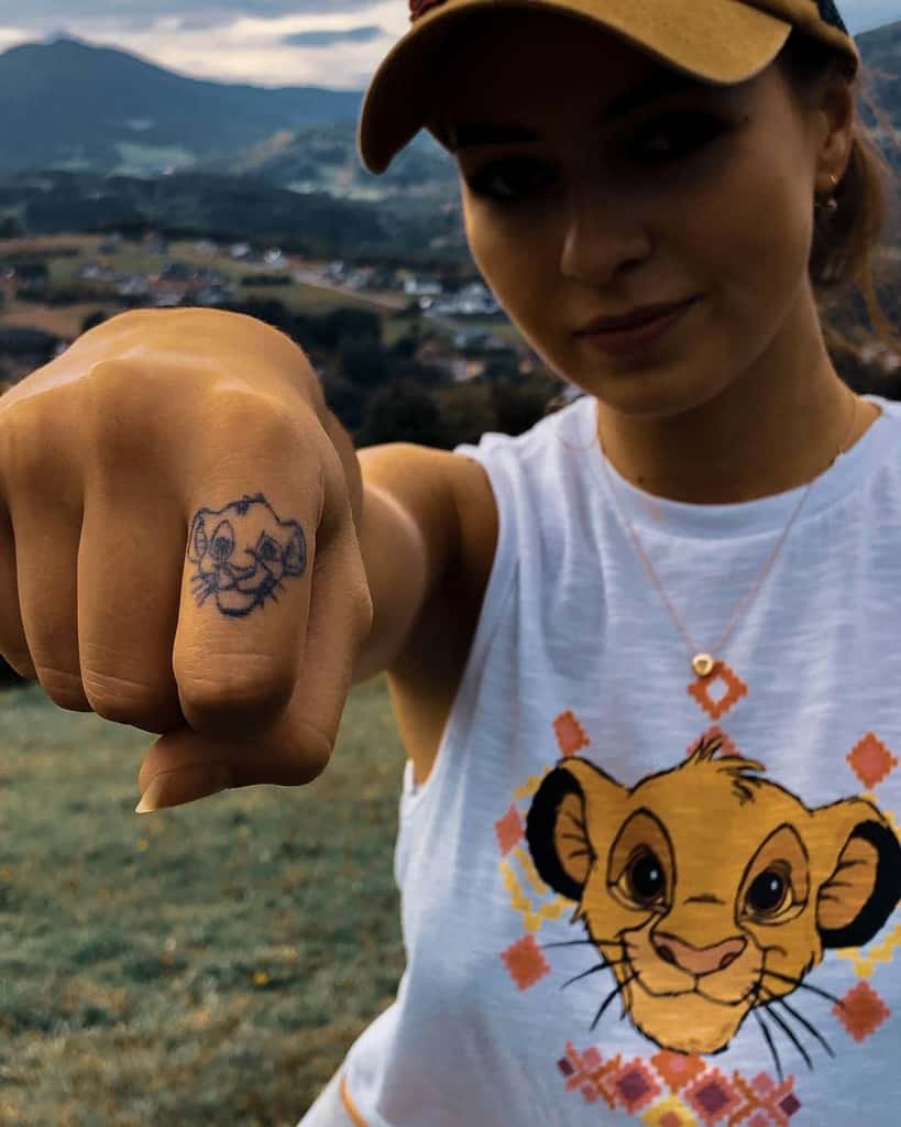 Close-up of a hand tattoo featuring Simba’s face on the knuckles