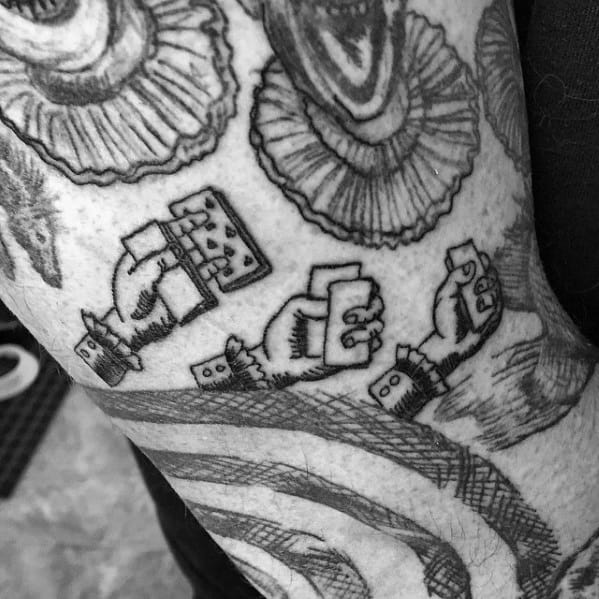 Black and white tattoo of three hands holding playing cards and dice, surrounded by detailed patterns