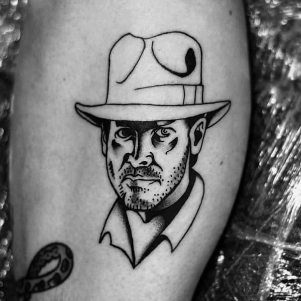 Black ink tattoo of Indiana Jones with bold linework, featuring his iconic fedora and rugged expression in a minimalist, sketch-style design.