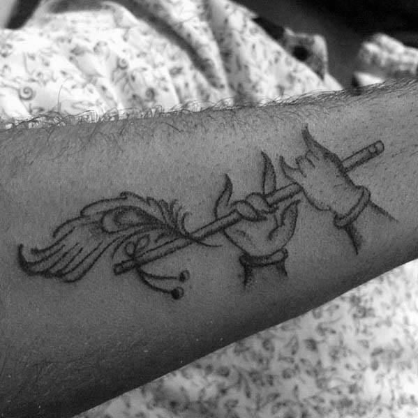 Blackwork Krishna tattoo showing two graceful hands holding a flute with a detailed peacock feather wrapped around it.