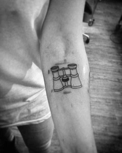Minimalist binoculars tattoo on the forearm with fine line details, symbolizing curiosity, exploration, and vision.