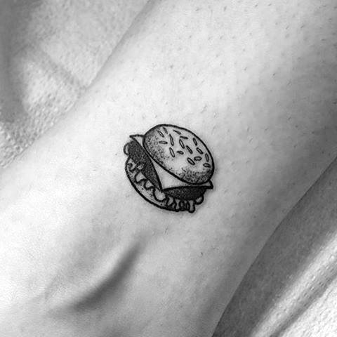 Cheeseburger tattoo design on ankle with sesame seed bun, cheese, and lettuce in minimalist black ink style