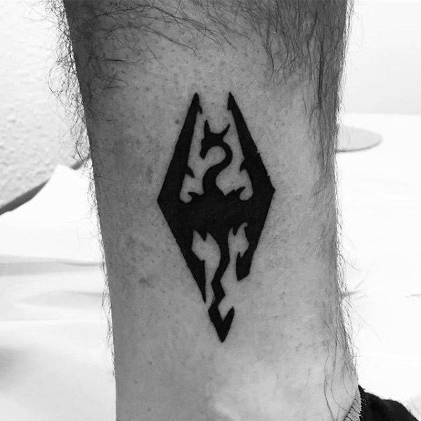 Simple black Skyrim dragon emblem tattoo inked on the lower leg, featuring bold lines and clean shading