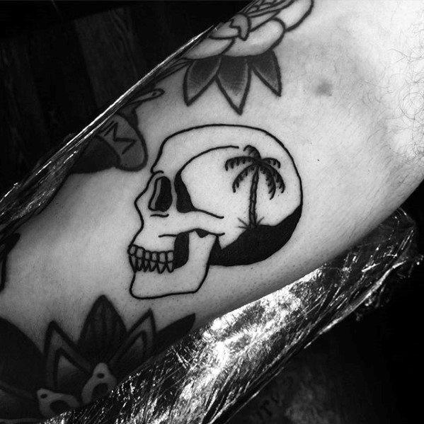Minimalist skull tattoo with a silhouette of a palm tree and sunset scene inside the skull, blending tropical calm with dark contrast.