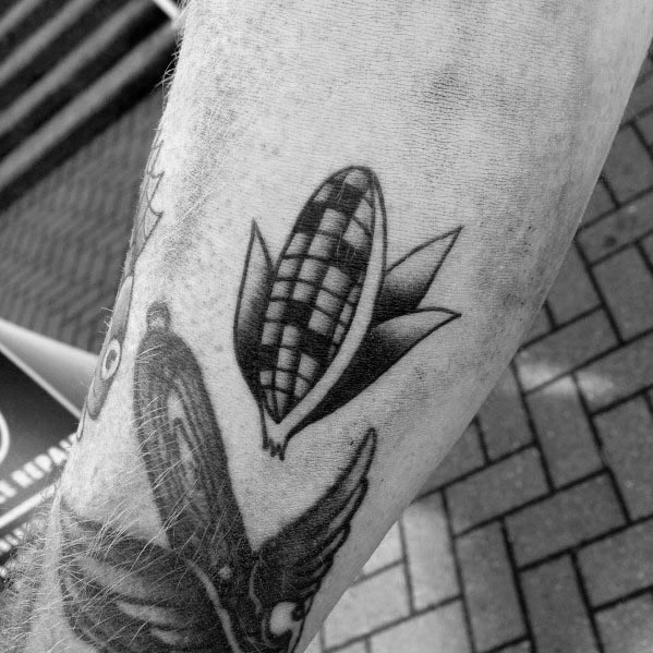 Minimalist black ink tattoo of a stylized corn cob with bold shading and simple geometric details on the forearm.