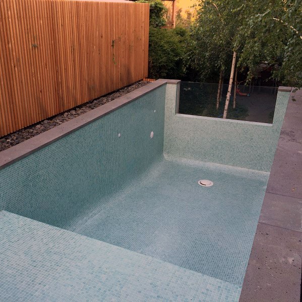 Minimalist small pool with soft green mosaic tiles and sleek wooden privacy fence.
