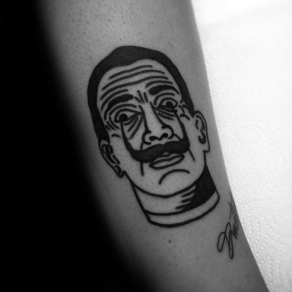 Minimalist blackwork tattoo of Salvador Dali with bold outlines, exaggerated facial features, and a stylized signature for a modern graphic look.