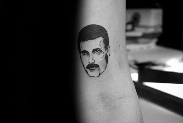 Simple blackwork tattoo of Freddie Mercury’s face with defined features and bold expression, placed on the inner arm.