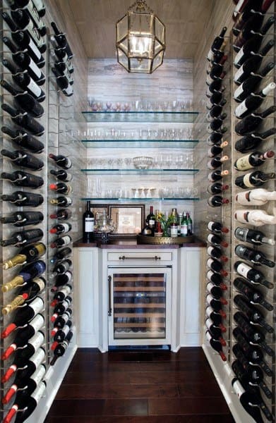 Small wine cellar with wall-mounted wine racks, a fridge, and glass shelves with bottles and glasses