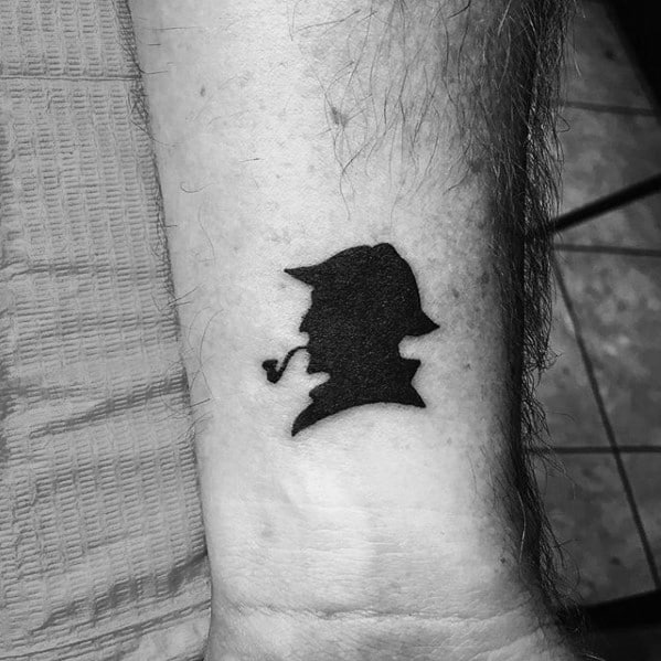 Black tattoo of Sherlock Holmes' silhouette with a pipe on a person's forearm