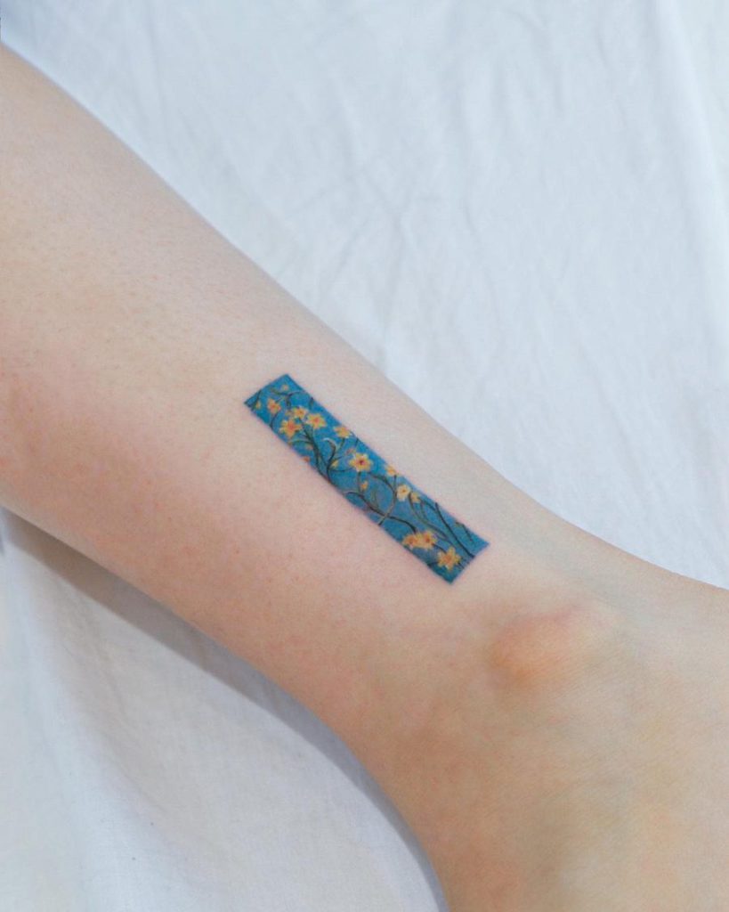 A minimalist tattoo of a rectangular blue background adorned with delicate yellow daffodils, capturing a subtle, floral design.