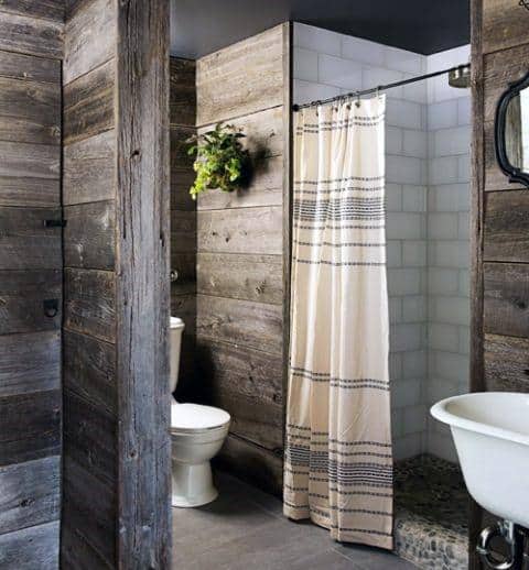 Rustic bathroom with wood walls, white fixtures, and a quaint striped shower curtain