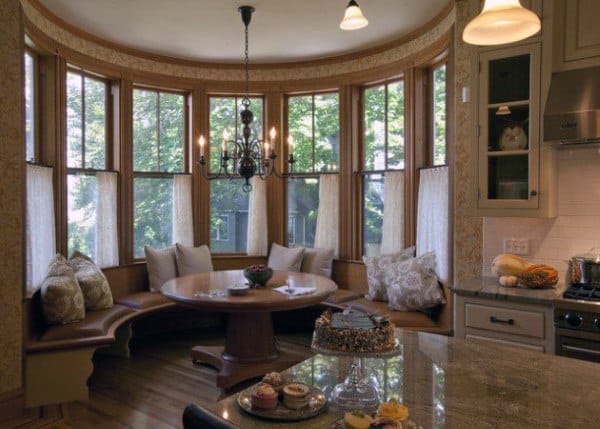 Cozy nook with curved windows, cushioned seating, and a round table set with desserts in a kitchen