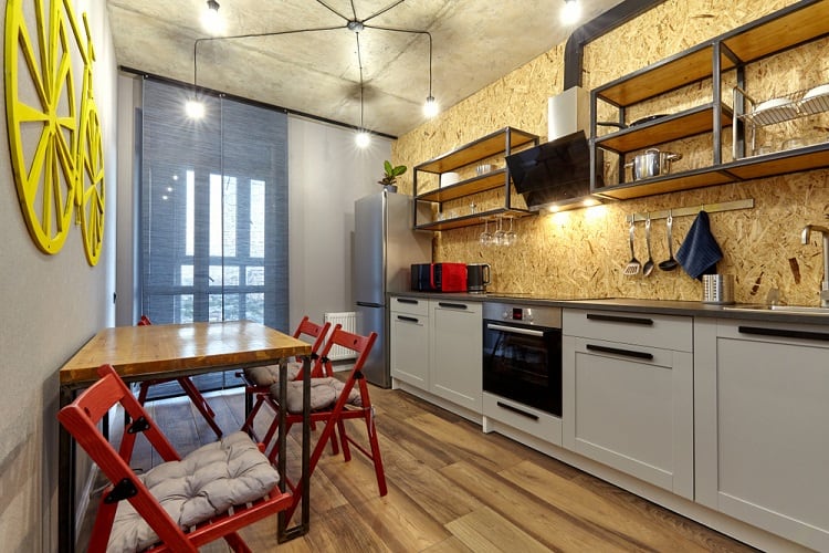 Small modern kitchen with an industrial style, featuring an unfinished ceiling, open shelving, and bright red chairs