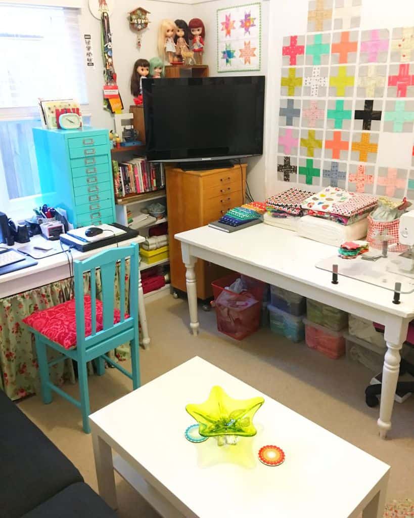 A colorful sewing room with organized storage, a crafting table, bright decor, and vibrant fabric stacks
