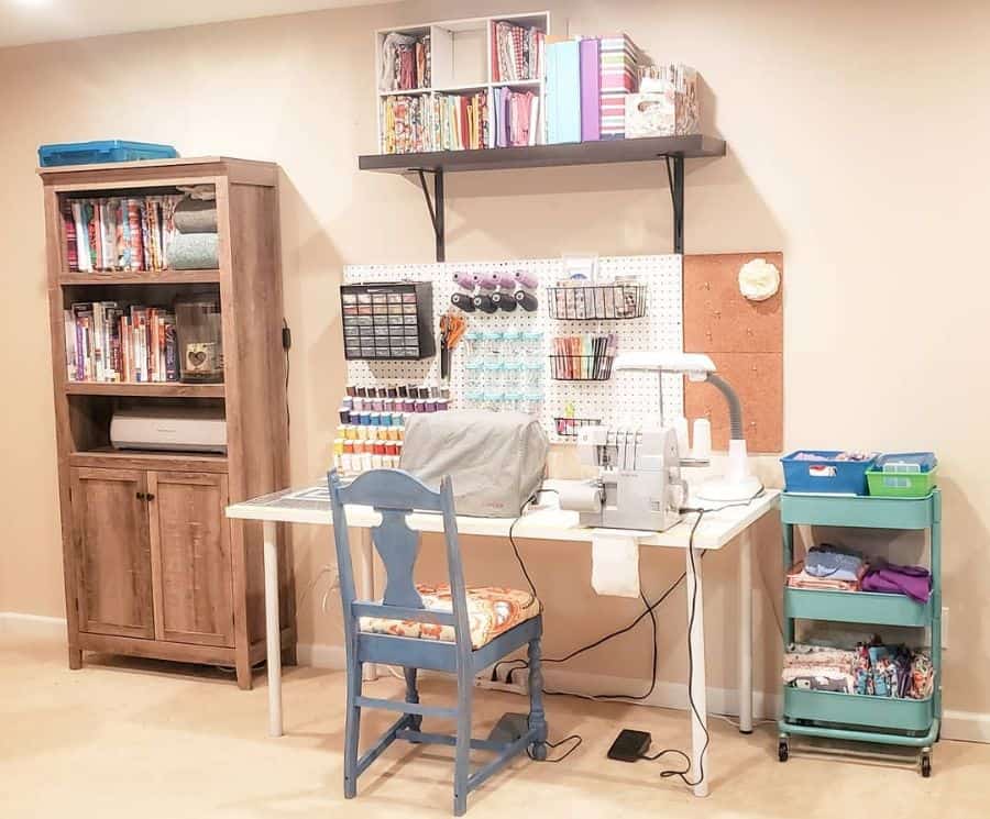 Organized sewing space with a serger, pegboard for tools, fabric cart, bookshelf, and overhead storage for supplies