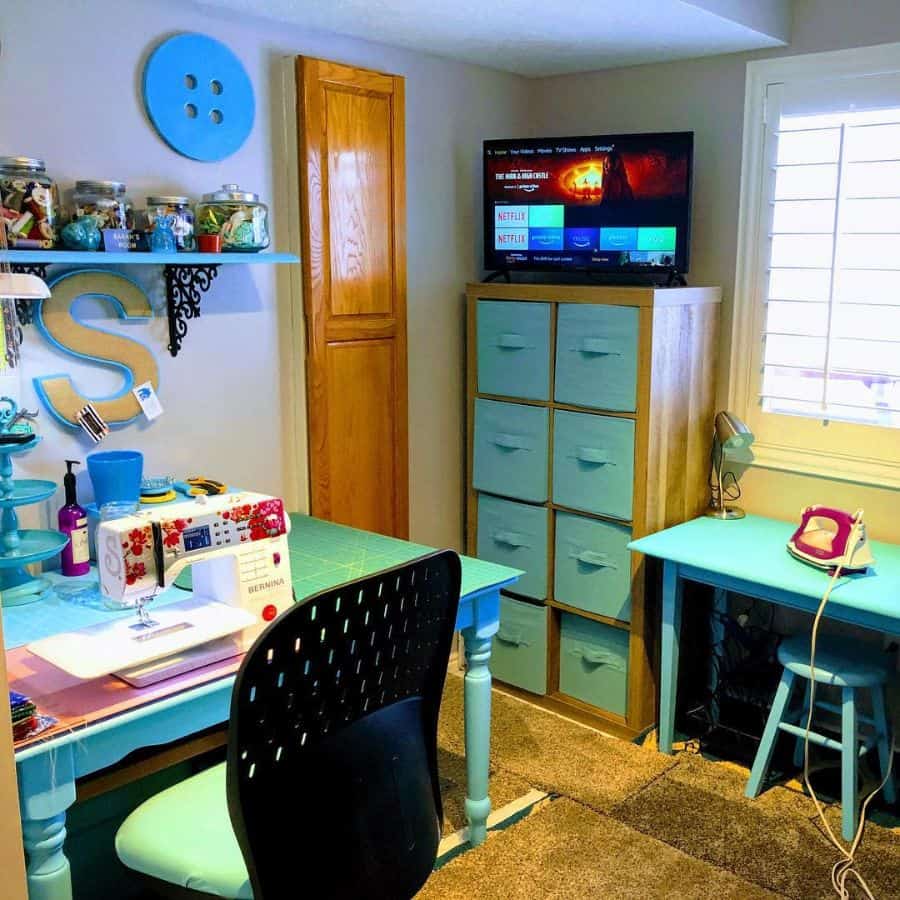 Bright sewing room with a turquoise desk, storage bins, TV, organized jars, and a cozy workspace for crafting