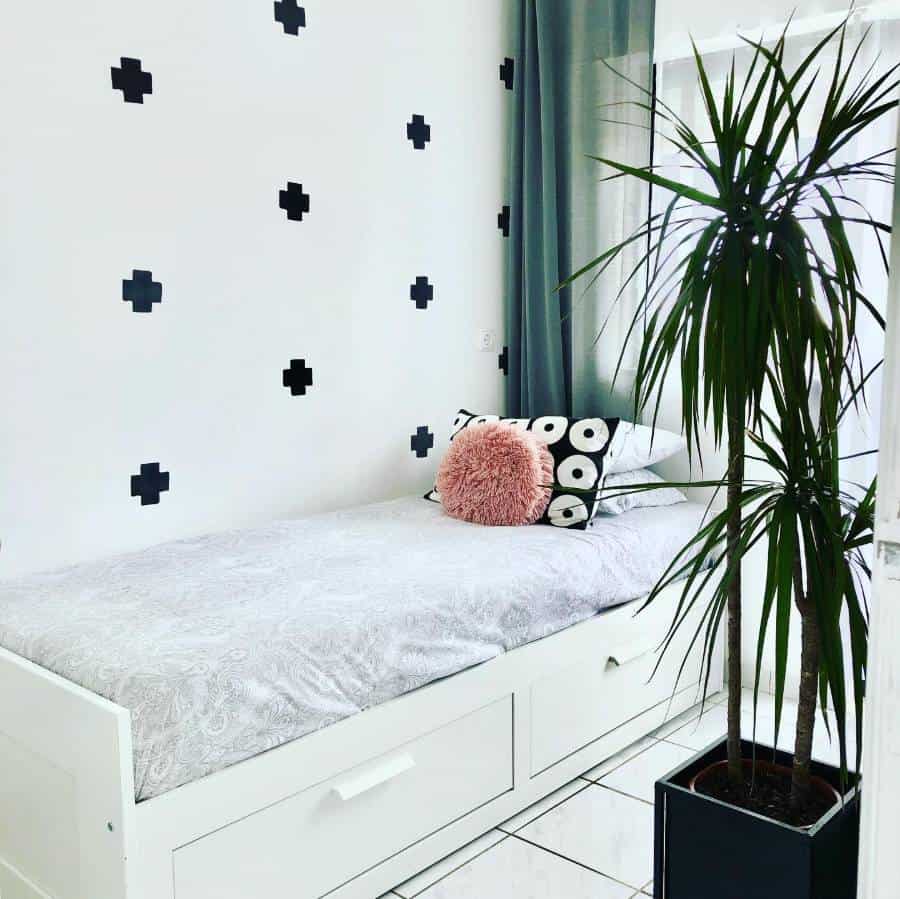 Minimalist white bedroom with a single bed, decorative pillows, patterned wall, and a tall potted plant