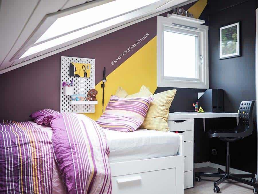 Cozy attic bedroom with striped bedding, yellow accents, and a small desk under a slanted skylight