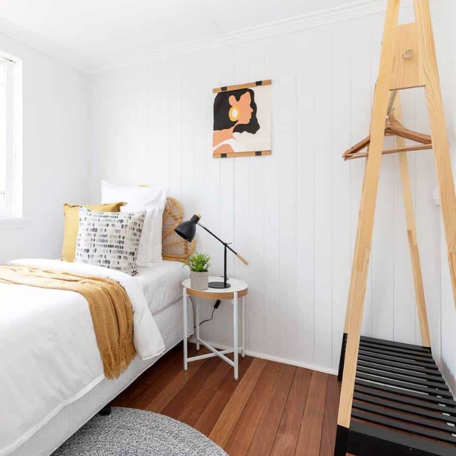 Minimalist white bedroom with wooden clothes rack and bedside table.