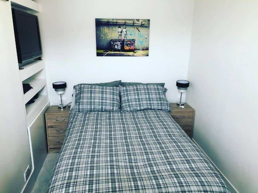 Small bedroom with plaid bedding, wall art, and bedside tables with lamps.