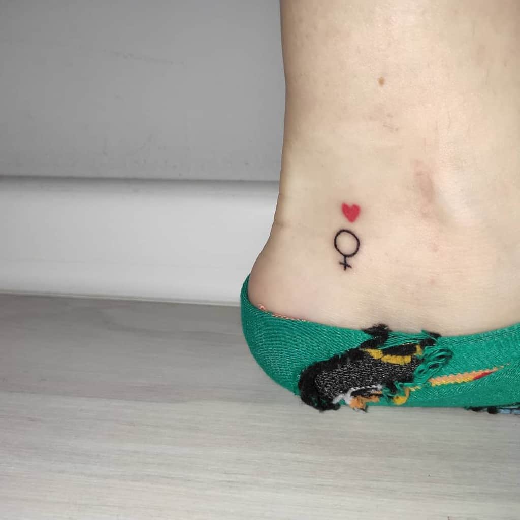 Minimalis tattoo featuring a small black Venus symbol with a tiny red heart above it, representing femininity and love