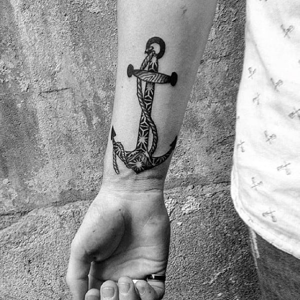Black-and-white tattoo of an intricately designed anchor on a person's inner forearm