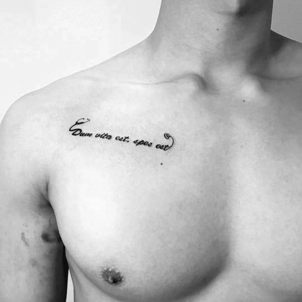 Latin script tattoo on the upper chest reading "Dum vita est, spes est," meaning "While there is life, there is hope," symbolizing resilience and optimism.