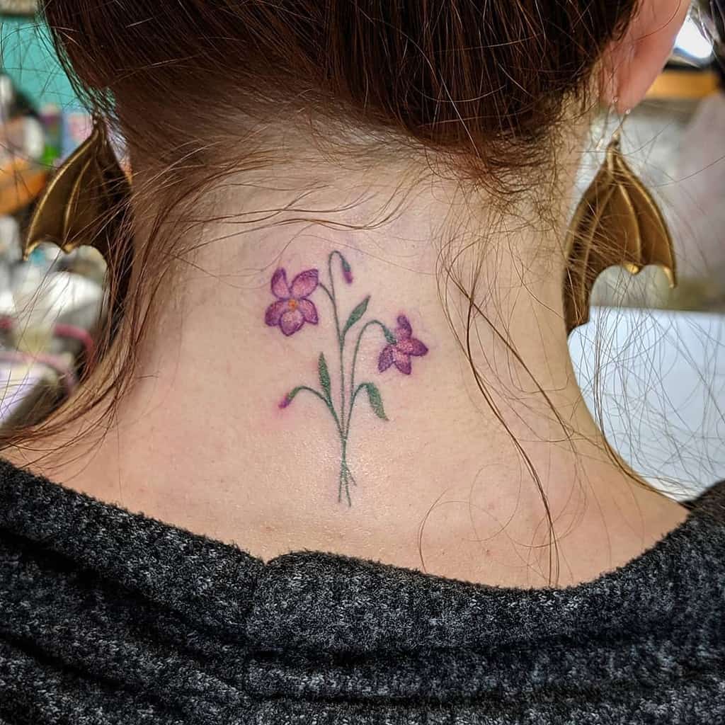 Delicate back-of-the-neck tattoo featuring two small violet flowers with fine green stems, symbolizing elegance, growth, and simplicity