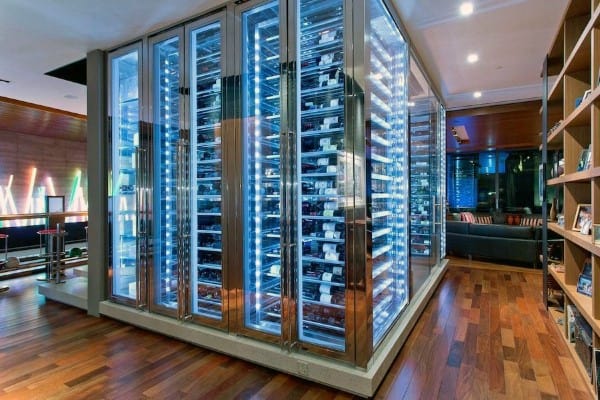 A sleek wine cellar with numerous bottles, illuminated by blue lighting in a modern room with wooden floors
