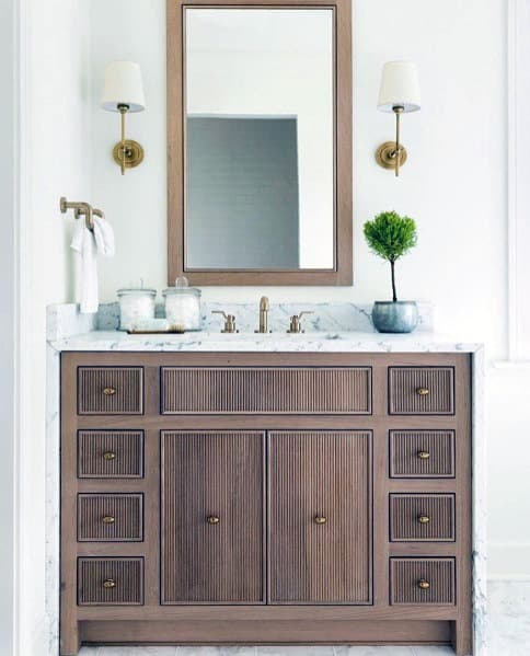Small wood bathroom vanity with marble countertop, single mirror, and brass accents.