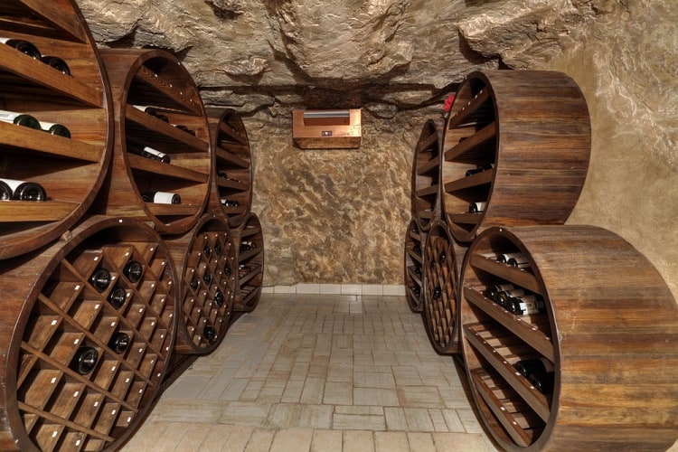 Underground wine cellar with round wooden racks and rustic stone walls.