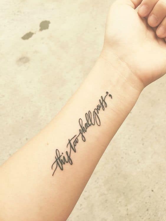 "this too shall pass" tattoo in cursive on the forearm.