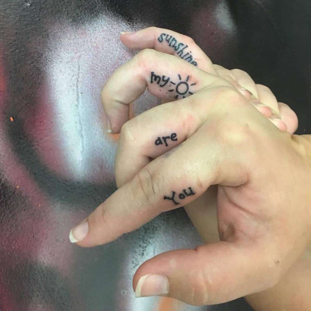 Hand with finger tattoos reading "sunshine," "my," "are," and "You" with a sun symbol