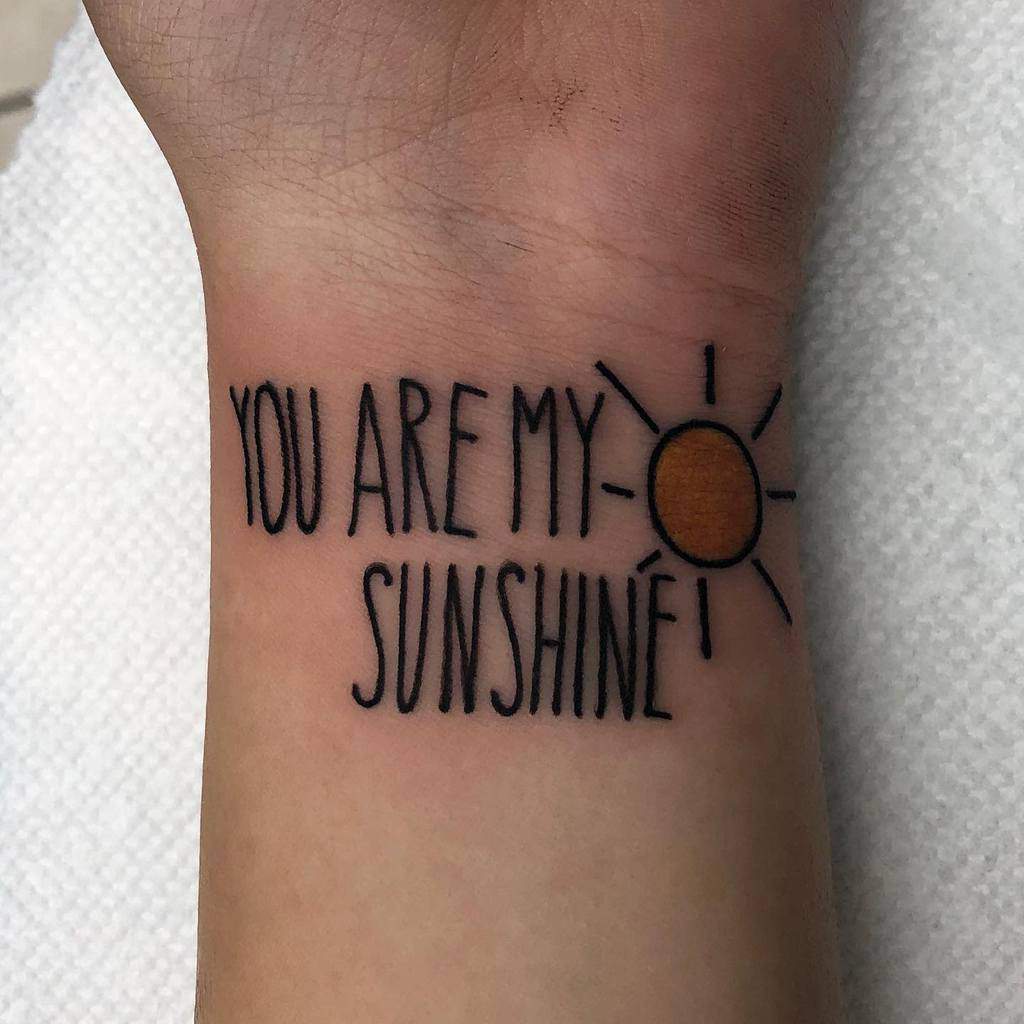 Wrist tattoo with "You Are My Sunshine" and a small sun design