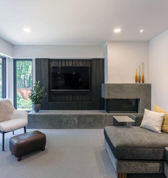 Modern living room with smooth concrete corner fireplace, wall-mounted TV, gray chaise sectional sofa, and white accent chair.
