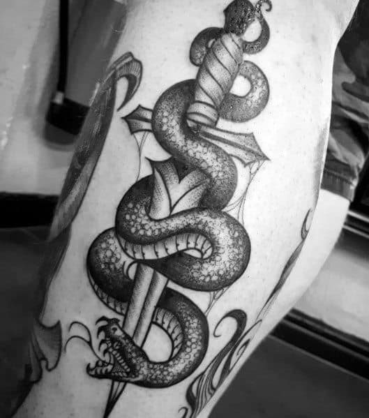 Black and grey snake and dagger tattoo on thigh, featuring intricate shading, fine details, and a bold traditional design.