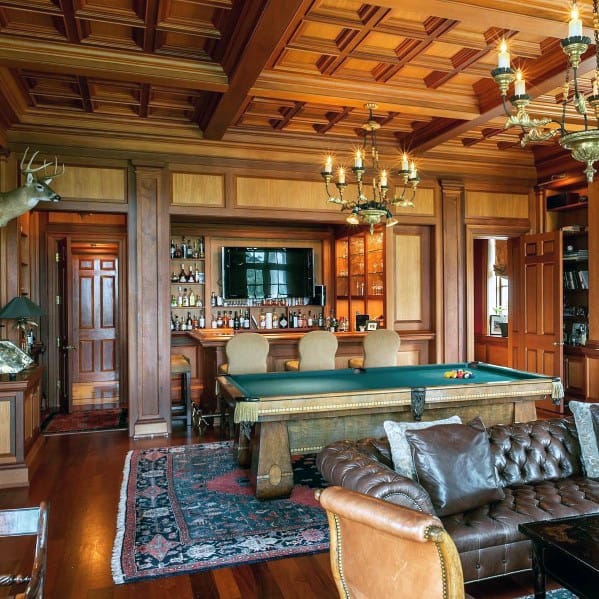 Elegant billiard room with coffered ceiling, leather seating, and a bar with classic wood finishes.