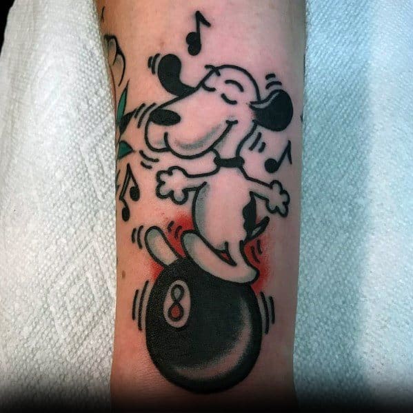 Colorful tattoo of Snoopy joyfully dancing on a magic 8-ball, surrounded by musical notes, placed on a person's forearm.