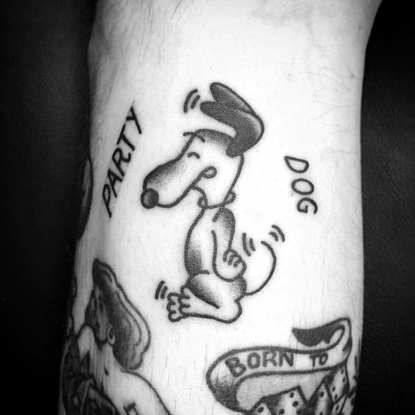 Black and white tattoo of Snoopy dancing with motion lines, surrounded by the words "PARTY DOG," placed on a person's arm.