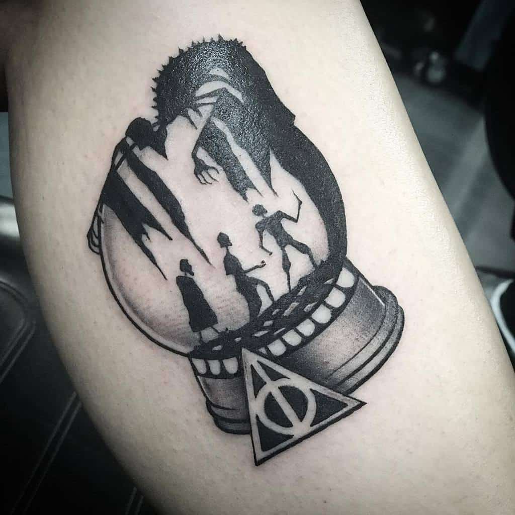 Black ink Deathly Hallows tattoo featuring a snow globe with the Tale of the Three Brothers scene inside, detailed shading, and bold lines.