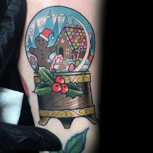 Christmas tattoo of a festive snow globe featuring a gingerbread man, candy canes, a decorated gingerbread house, and holly for a whimsical holiday design.