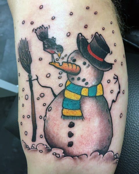 Charming snowman tattoo with a top hat, striped scarf, broom, and a bird nibbling on its carrot nose, capturing a playful winter scene.