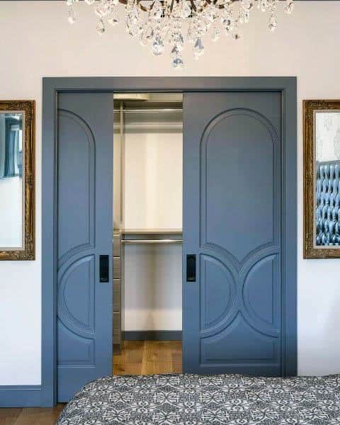 Elegant blue closet doors slide smoothly, flanked by framed mirrors under a sparkling crystal chandelier