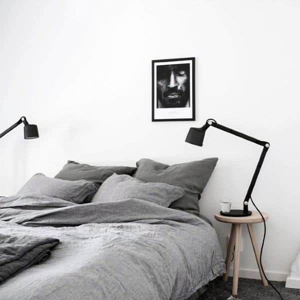 Minimalist bedroom with a grey bed, two black lamps, and a framed black-and-white portrait on a white wall