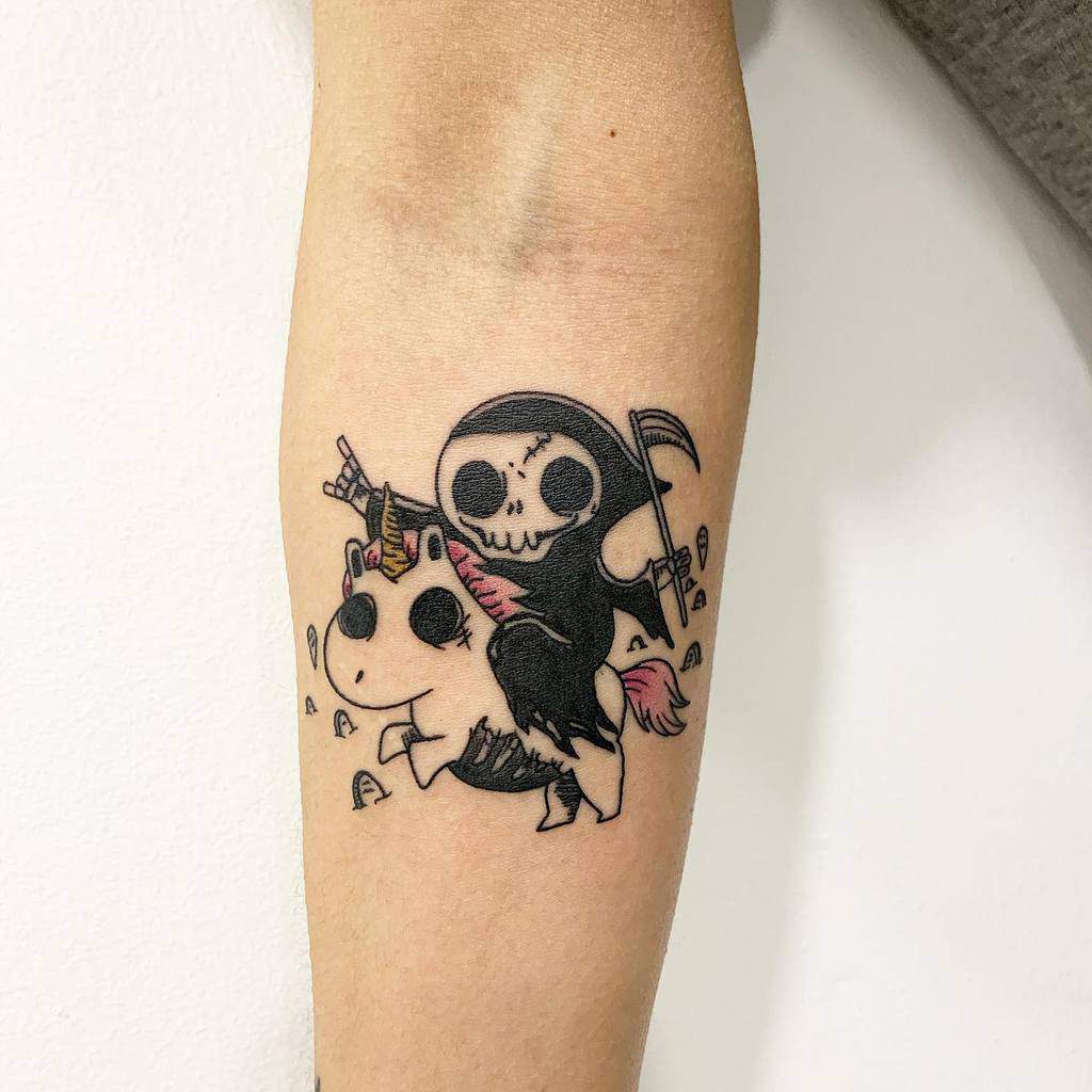 Playful tattoo of a cute Grim Reaper riding a unicorn, holding a scythe and making a rock hand gesture, surrounded by tiny bones.