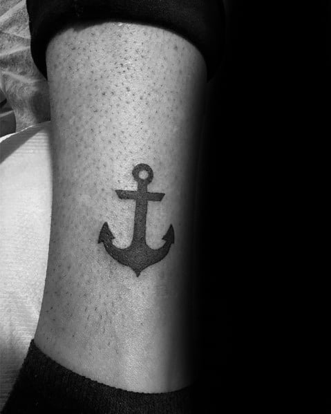 Small black anchor tattoo on the leg with a bold, simple design, symbolizing stability, strength, and a deep connection to the sea.