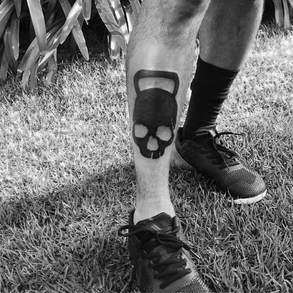 Bold black kettlebell skull tattoo on the shin, symbolizing strength, resilience, and a hardcore dedication to fitness and CrossFit training.