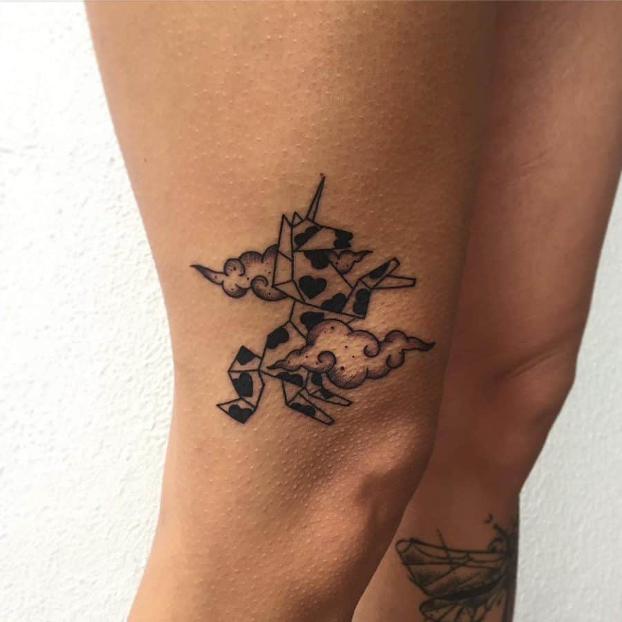 Small black ink tattoo of an origami-style unicorn with playing card patterns, surrounded by clouds, blending fantasy and geometric design.