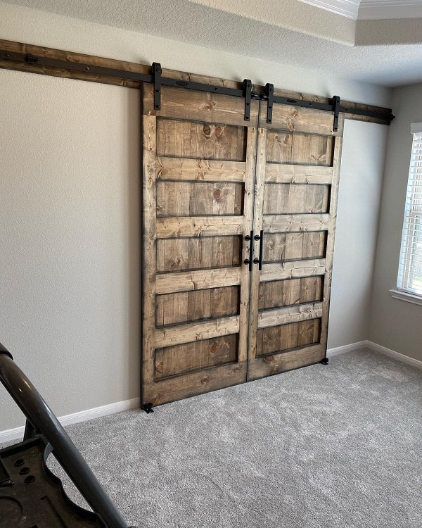 Solid wood double sliding barn doors with black hardware in a modern carpeted room.